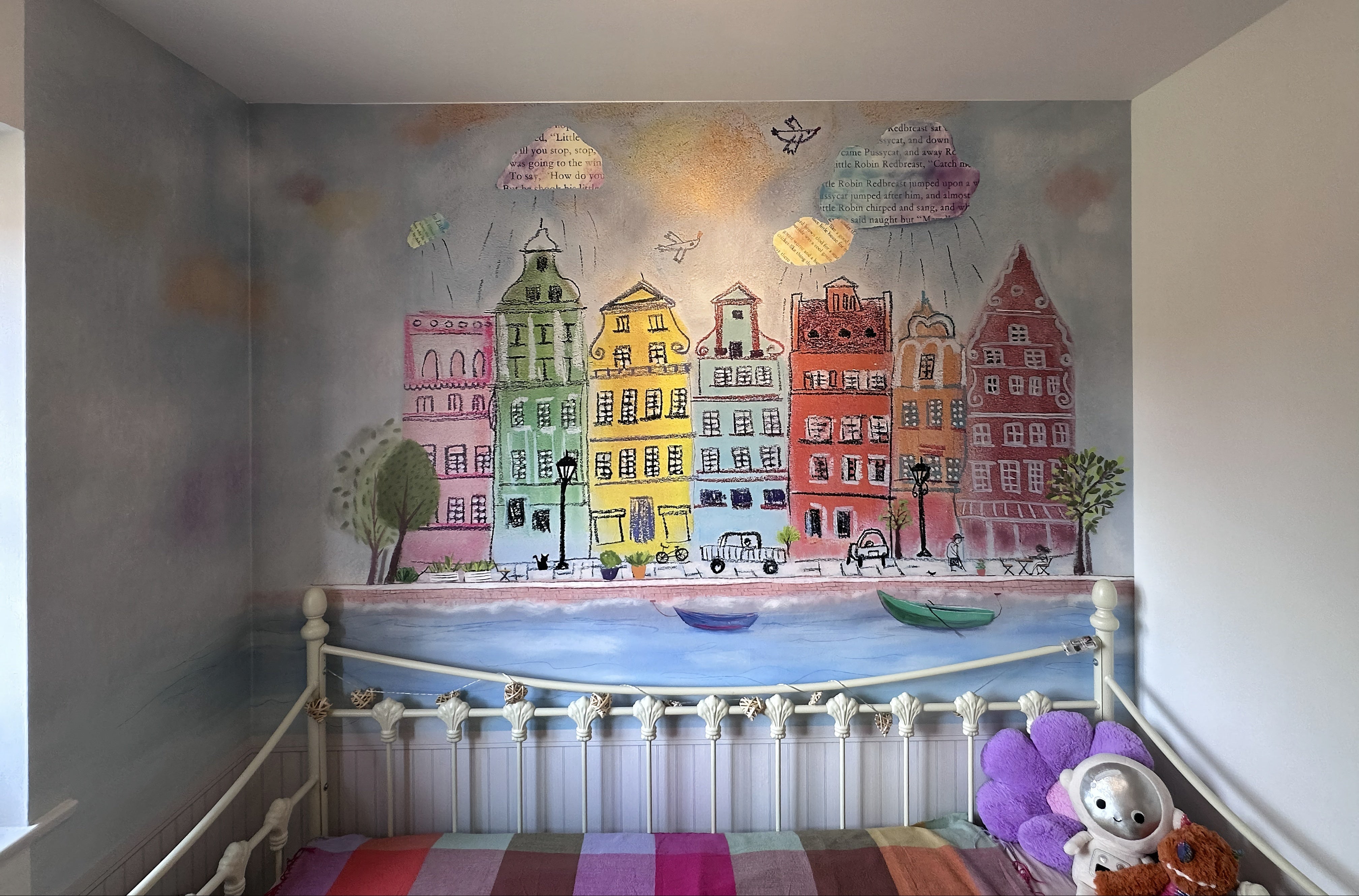 A colorful hand-painted mural of European canal houses and boats on a bedroom wall above a white bed frame.